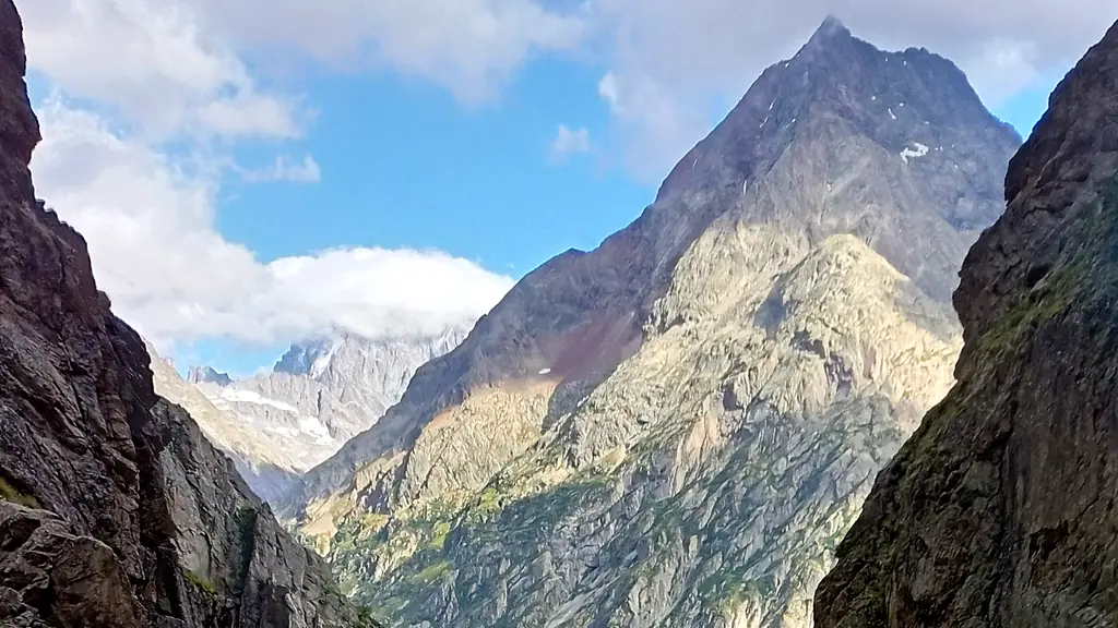 A rocky alpine valley between dark cliffs, a sharp sunlit peak at its head under broken cloud
